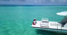 Man And Woman Sit On Back Of Boat And Fish Together In The Tropics, Aerial Zoom In Shot