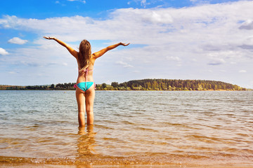teen girl with raised hands stands in the water of a beautiful lake at summer vacations