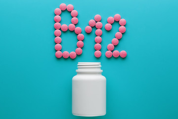 Pink pills in the shape of the letter B12 on a blue background, spilled out of a white can.