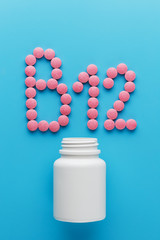 Pink pills in the shape of the letter B12 on a blue background, spilled out of a white can.