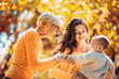 © Mediteraneo - Grandmother and mother smiling at baby in autumn park.