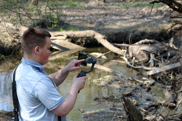 Wall Mural - A young man videotaping on a smartphone. Uses gimbal to get smooth footage. Closely watching the movie shooting.