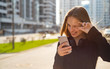 © pavel siamionov - Outdoor portrait of young teenager brunette girl with long hair. girl on city in black dress looking on the smart phone walking in the street in a sunny day