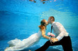 The beautiful bride and groom hold hands and kiss underwater at the bottom of the pool on a Sunny day. Portrait. Concept. Underwater wedding. Horizontal view