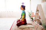 mindfulness, spirituality and healthy lifestyle concept - woman meditating in lotus pose at yoga studio with seven chakra symbols