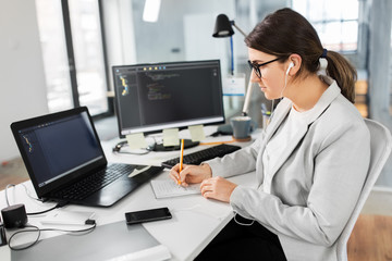 business, technology and people concept - businesswoman in earphones with notebook and computers working at office