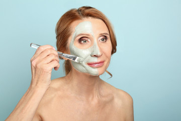 Mature woman applying facial mask against color background