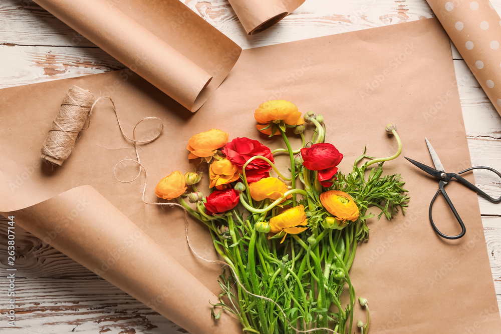 Beautiful flowers with scissors and wrapping paper on wooden table
