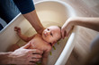 © Halfpoint - Unrecognizable parents giving a newborn baby a bath at home.