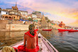 Varanasi city architecture with Ganges river bank at sunset with view of Hindu sadhu enjoying a boat ride on river Ganga.