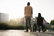 © Santi Nunez/Stocksy - Back view of woman on wheelchair and her boyfriend using crutches