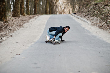 Wall Mural - Street style arab man in eyeglasses with longboard longboarding down the road.