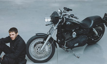 Man Sitting On The Floor Next To His Motorcycle In The Garage