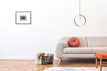 Stylish minimalistic living room with design grey sofa,  geometric lamp, retro footrest, basket with blanket and elegant accessories Mock up posters frame on the white walls. Minimalistic home decor. 