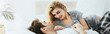© LIGHTFIELD STUDIOS - panoramic shot of cheerful blonde girl looking at boyfriend lying on pillow in bedroom