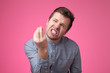 © RealPeopleStudio - Handsome young man looking angry showing italian gesture over pink background.