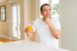 © Krakenimages.com - Middle age man drinking a glass of orange juice at home serious face thinking about question, very confused idea