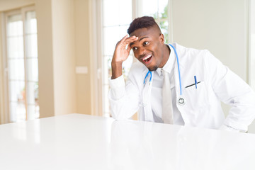 Canvas Print - African american doctor man at the clinic very happy and smiling looking far away with hand over head. Searching concept.