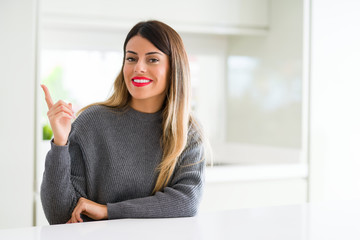 Young beautiful woman wearing winter sweater at home with a big smile on face, pointing with hand and finger to the side looking at the camera.