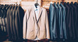 © golubovy - Men formal wear. Classy outfit. Modern clothing store. Business suit jackets and vests hanging, displayed over brick wall.