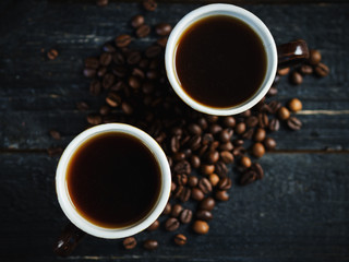 Two small cups of freshly brewed espresso on a wooden background with scattered coffee beans