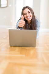 Poster - Beautiful young woman laying on the floor using laptop happy with big smile doing ok sign, thumb up with fingers, excellent sign