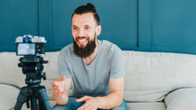 Social media influencer creating content. Smiling bearded hipster guy shooting video using camera on tripod.