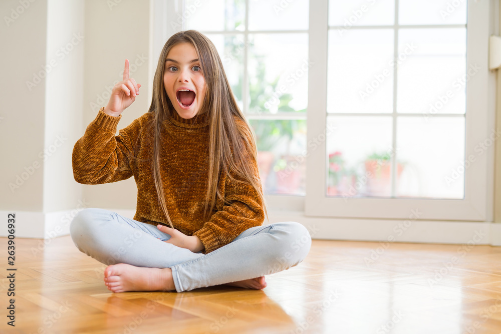 Beautiful young girl kid sitting on the floor at home pointing finger ...