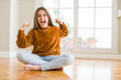 © Krakenimages.com - Beautiful young girl kid sitting on the floor at home very happy and excited doing winner gesture with arms raised, smiling and screaming for success. Celebration concept.