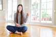 © Krakenimages.com - Beautiful Asian woman sitting barefoot on the floor at home with a big smile on face, pointing with hand and finger to the side looking at the camera.