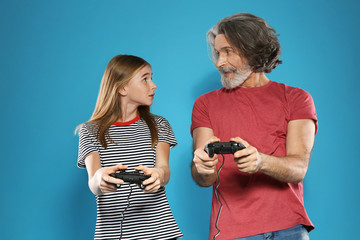 Wall Mural - Mature man and teenage girl playing video games with controllers on color background