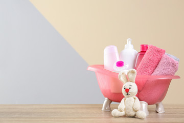 Wall Mural - baby cosmetic products, knitted rabbit and towels on table against color background. space for text