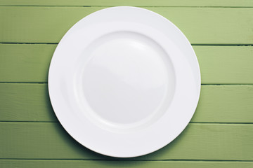 Poster - White plate and a fork with a spoon on a green wooden table background.