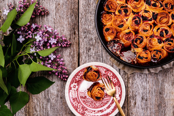 Wall Mural - Homemade mini cherry rolls in a baking form and two rolls on a plate with bouquet of lilac on vintage wooden table. Bun cake with cherry filling