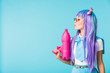 Asian anime girl in wig and glasses holding water gun isolated on blue
