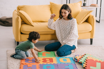 Wall Mural - Mother and son playing with alphabet puzzle mat on carpet