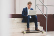 © Westend61 - Happy young businessman with skateboard sitting outdoors on stairs using laptop