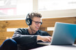 © Westend61 - Smiling young man using laptop listening to music with headphones