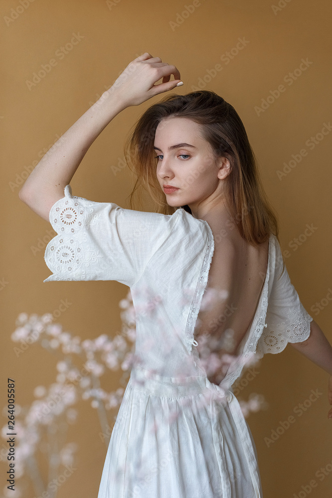 Beautiful young girl with long hair in white dress posing on beige ...