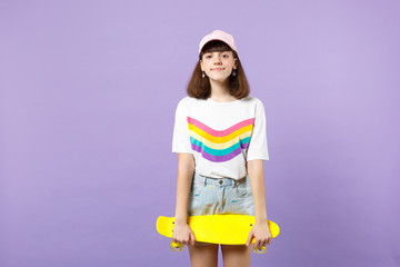 Wall Mural - Portrait of smiling teen girl in vivid clothes looking camera, holding yellow skateboard isolated on violet pastel background in studio. People sincere emotions, lifestyle concept. Mock up copy space.