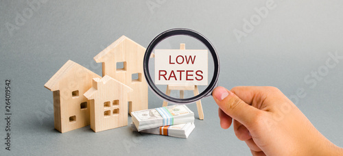 Cuadros en Lienzo A magnifying glass is looking at a poster with the word Low rates and wooden house