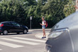 Schoolgirl with headphones and mobile phone on pedestrian crossing in front of a car