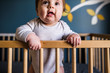 © Cavan Images - close up of drooling baby standing and leaning against crib rail