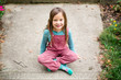 © Cavan Images - Portrait of a happy little girl sitting on the sidewalk smiling