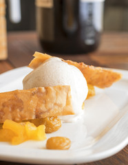 The ball of white vanilla ice cream with 2 waffles and mango fruit embellished with few risens. White plate on wooden table.