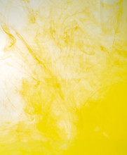 Yellow Acrylic Paint Dissolving Into Water, Close Up View. Blurred Background. Yellow Abstract Pattern Of Ink In Liquid. Acrylic Clouds Mixing With Water, Abstract Background
