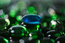 Blue Glass Stone Pebble Sitting On Green Glass Stone Pebbles With Other Blurred Pebbles