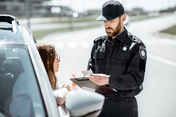 Poster - Policeman checking documents of a young female driver standing near the car on the roadside in the city