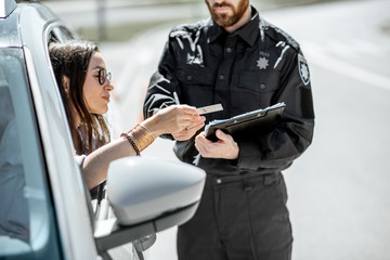 Poster - Policeman checking documents of a young female driver standing near the car on the roadside in the city