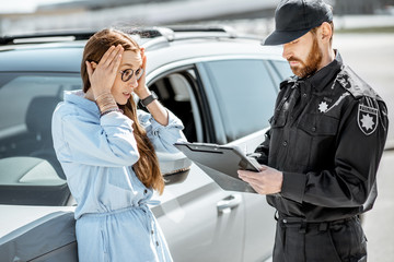 Poster - Policeman standing with upset female driver while issuing a fine for violating the traffic rules on the roadside near the car